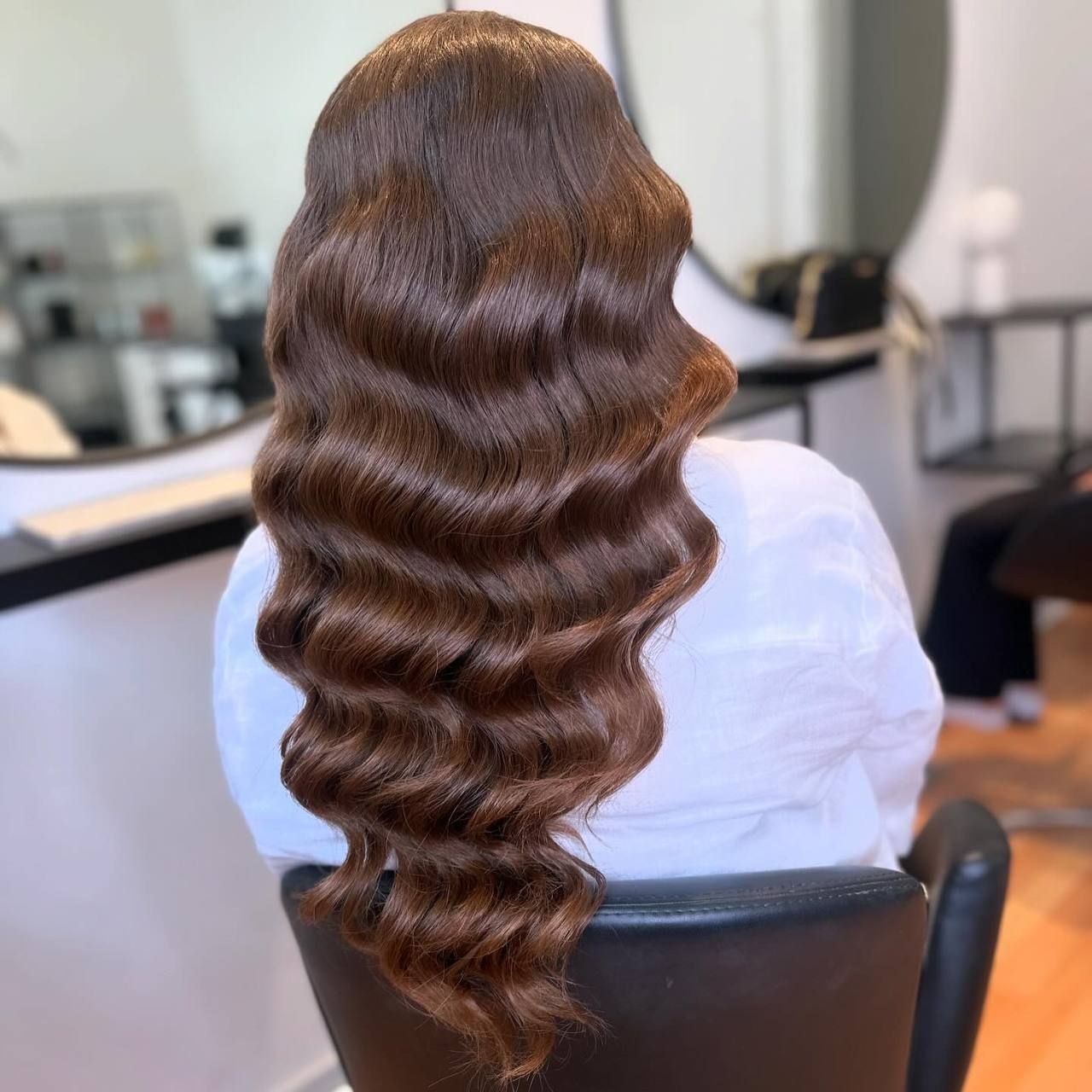 Person with long, wavy brown hair sitting in a salon chair.